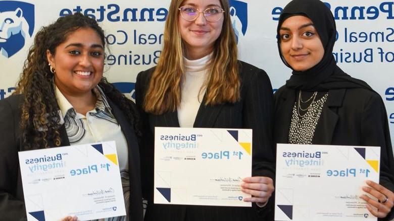 Three female students pose in front of a Penn State Smeal College of Business backdrop holding 1st place certificates